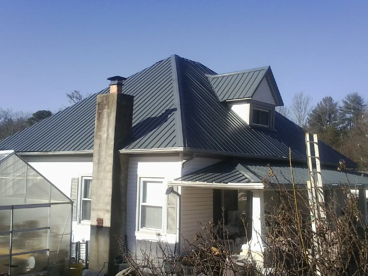 Dark blue standing seam metal roof on a white farmhouse with dormer — Slate & Tile Roof Repair by Roofing Brothers in Saint Cloud