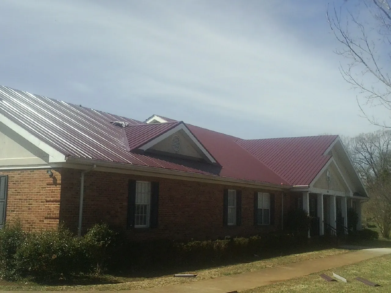 Red metal roof with gabled entries on a long brick building, from a Hail Damage Roof Repair job in Saint Cloud